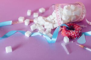 Creative representation of sugar consumption using cubes, donut, ribbon, and syringe.