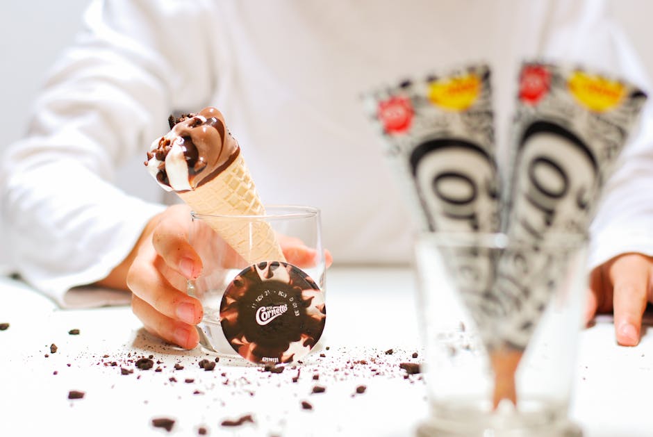 A tempting chocolate ice cream cone held by a person in a white shirt, surrounded by Oreo wrappers and chocolate crumbs.