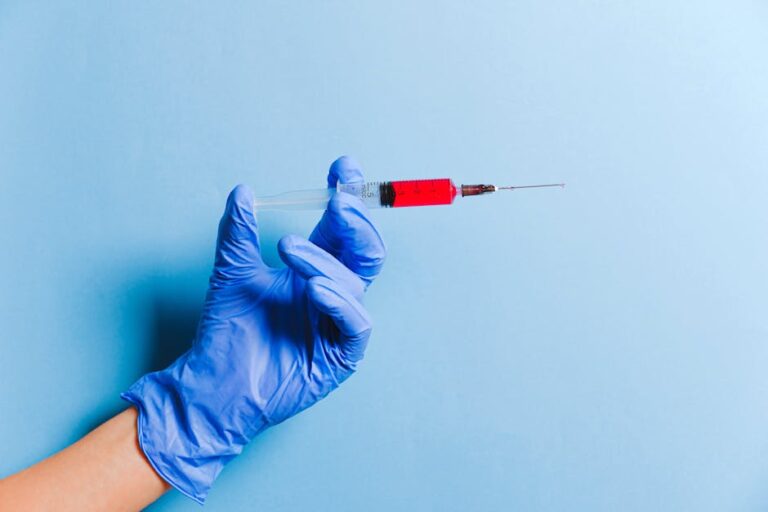 Close-up of a gloved hand holding a syringe with red fluid against a blue background, symbolizing healthcare and medicine.