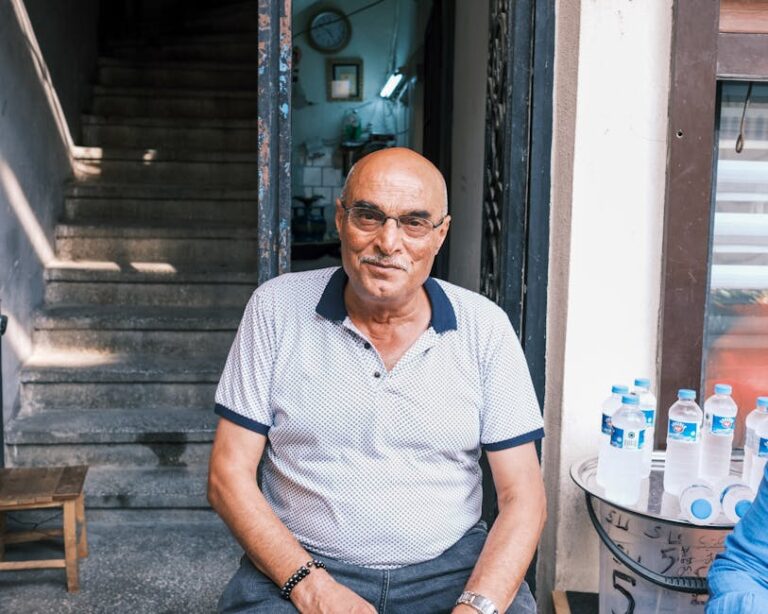 Elderly man sitting outdoors by stairs, smiling warmly at a café entrance.