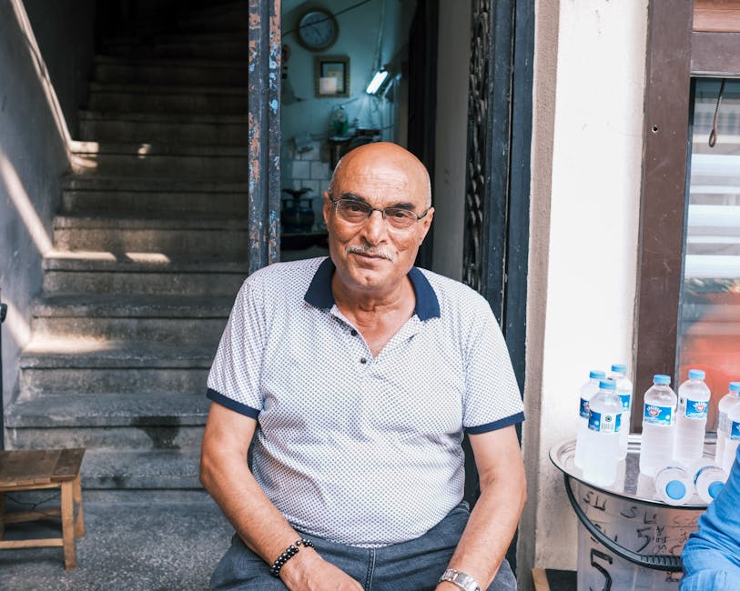 Elderly man sitting outdoors by stairs, smiling warmly at a café entrance.