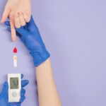 Gloved hand testing blood glucose level with meter and blood drop.