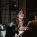 A dramatic scene of two adults in a dimly lit interrogation room, captured from a unique angle.