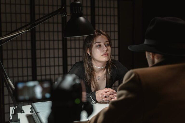 A dramatic scene of two adults in a dimly lit interrogation room, captured from a unique angle.