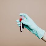 Close-up of a gloved hand holding blood test tubes against neutral background.