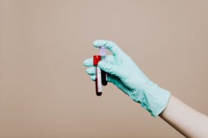 Close-up of a gloved hand holding blood test tubes against neutral background.