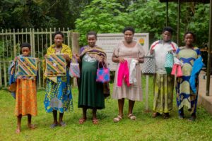 A group of African women showcasing colorful handmade crafts outdoors at Bwindi Community Hospital.