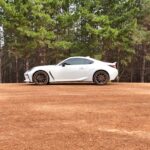 A sleek white sports car parked on a dirt road amidst a lush green forest setting in Perth, Australia.