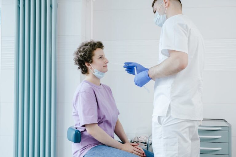 Healthcare worker performs a COVID-19 swab test on a seated patient indoors.