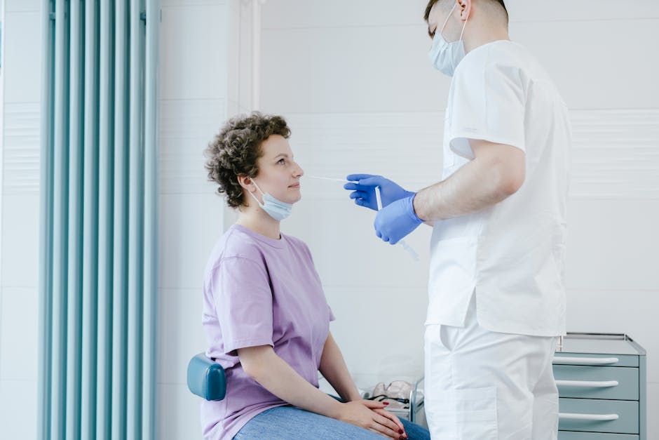 Healthcare worker performs a COVID-19 swab test on a seated patient indoors.