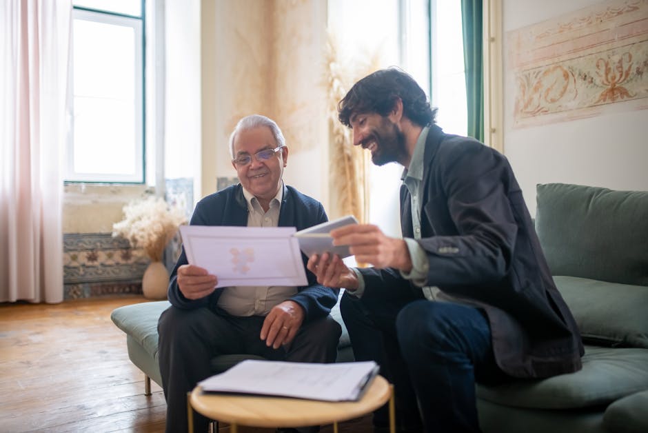 An elderly man and a younger man in a casual office setting, discussing documents with smiles.