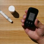 Close-up of a hand holding a blood glucose meter displaying results on a wooden table.