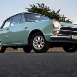 Low-angle view of a vintage blue classic car parked outdoors on an asphalt road at dusk.