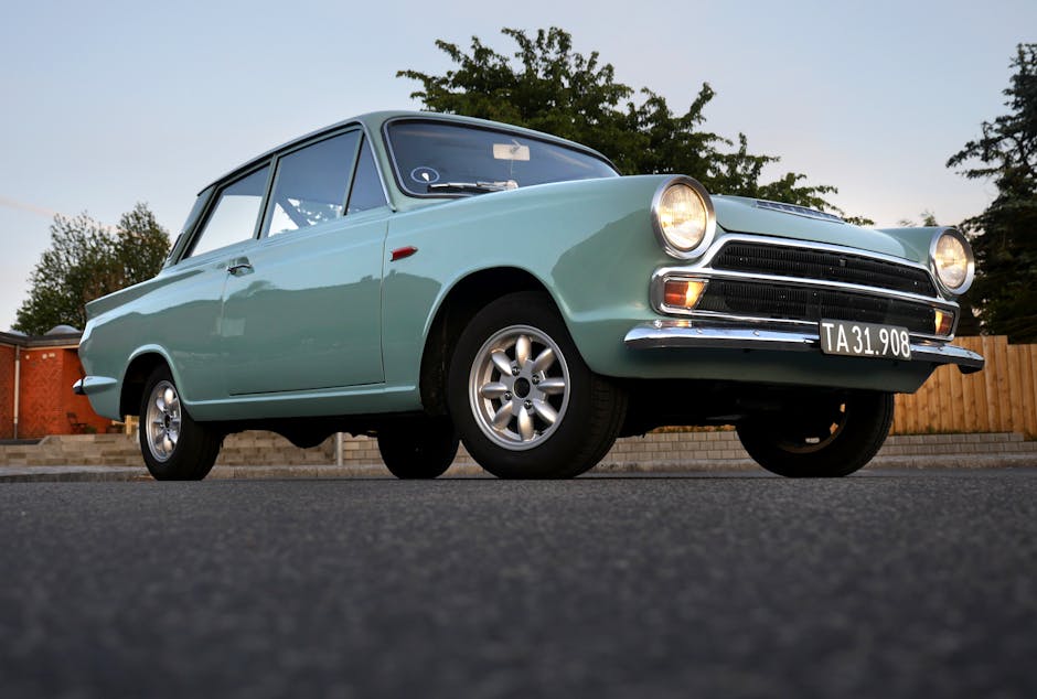Low-angle view of a vintage blue classic car parked outdoors on an asphalt road at dusk.