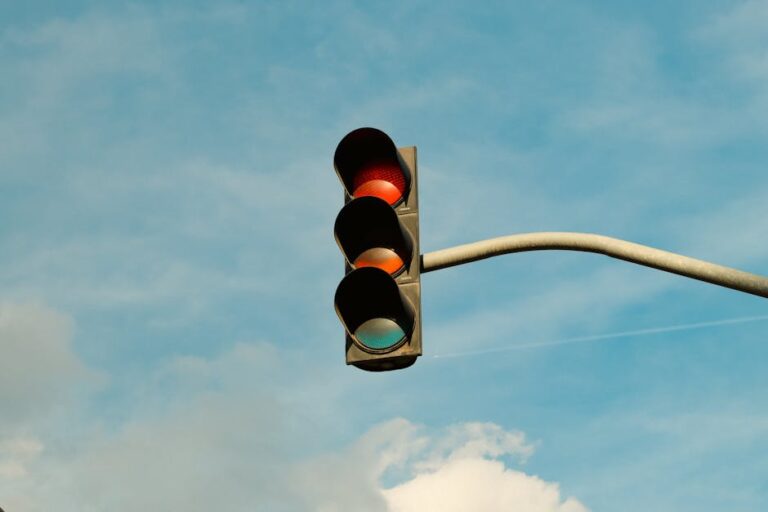 A traffic light with red signal set against a blue sky, signifying stop in urban streets.