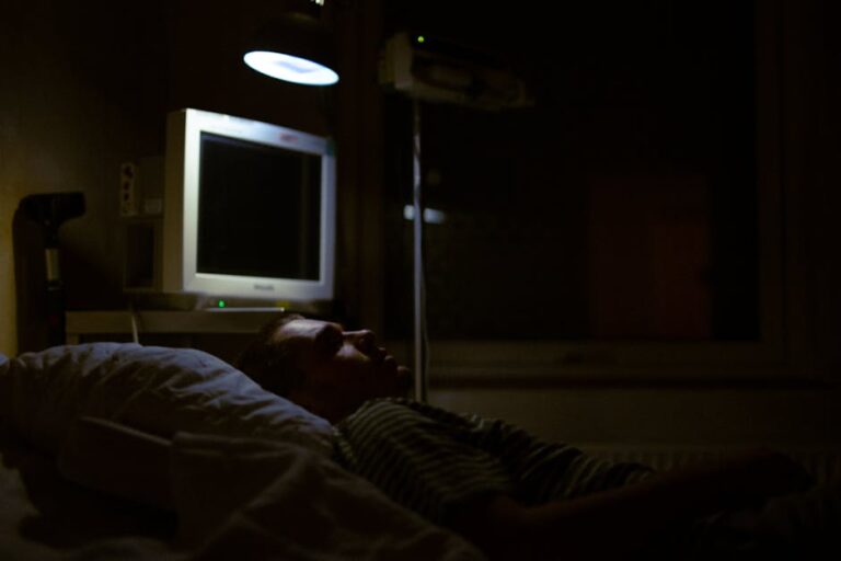 Man lying on a hospital bed under dim light, with medical equipment visible.