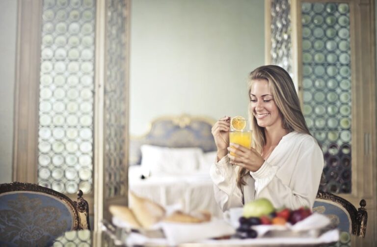 Woman enjoying a fresh breakfast with juice in a luxurious room showcasing comfort and relaxation.