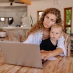 Mother and child using a laptop at home, working and bonding in a cozy environment.