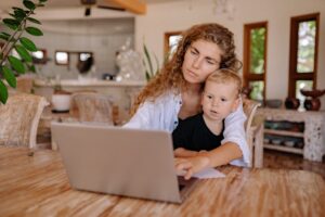 Mother and child using a laptop at home, working and bonding in a cozy environment.