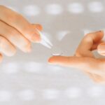 Close-up of female hands carefully handling a contact lens with a tweezer.