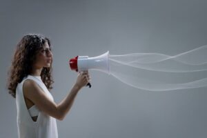 Woman using a megaphone emitting sound waves on a gray background.