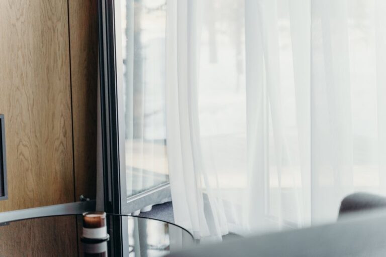 A modern hotel room with sheer curtains softly lit, emphasizing luxury and tranquility.