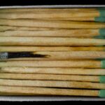A stack of matches in a box viewed from above, featuring one burnt match among the unused ones.
