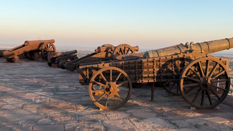 Row of historic cannons on a stone fortification at sunset.