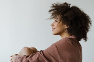 Portrait of a woman with curly afro hair sitting indoors, showcasing natural beauty and elegance in a studio setting.