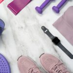 Flat lay of fitness gear including yoga mat, dumbbells, and smartwatch on a marble surface.