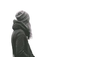 A woman in a winter jacket and beanie facing away on a plain background.