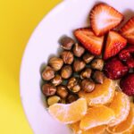 Close-up of a bowl with fresh fruits and nuts against a vibrant yellow backdrop.